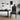 A modern dining room scene featuring a black dining table and a black chair with a white geometric tribal pattern, styled with a black desk lamp, a black pendant light, a woven rug, and a potted plant against a white wall.