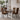 A modern dining set featuring a round gray table and four high-back chairs upholstered in a bold geometric patterned fabric with black, orange, and yellow tones, set in a contemporary dining room.
