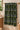 A folded towel or blanket with a bold geometric tribal pattern in black, lime green, and white, hanging on a brass towel bar in a bathroom setting.