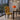 A modern dining chair with a bold yellow, black, and red geometric patterned upholstery, set in a contemporary dining room next to a wooden table and orange lamp.