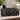 A folded black cotton towel with a white geometric and coffee-themed pattern sits on a white marble bathroom counter next to a sink, soap dispenser, and potted plant.