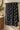 A black and white patterned bath towel hanging from a brass rod in a bathroom setting next to a vanity and plant.