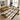A large rectangular area rug with a cream base and bold black, brown, and tan geometric diamond patterns is styled in a modern living room with a yellow sofa, two white armchairs, and decorative pillows.