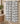 A white fabric towel or bath towel with a black geometric tribal pattern hangs from a brass rod in a bathroom setting.