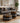 Two round ottomans with a geometric tribal pattern in black, white, and ochre yellow, styled in a modern living room next to a gray sofa.