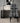 A modern dining chair with a bold black and white geometric pattern, positioned in front of a minimalist black desk and a gray concrete wall.