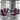 A modern dining room setup with a clear glass-top table and six matching chairs featuring a bold geometric pattern in magenta, black, orange, and white. The chairs are arranged around the table in a contemporary loft setting with concrete walls, large windows, and a hanging glass chandelier.