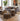 A styled living room scene featuring a gray fabric sofa with patterned throw pillows, two matching geometric ottomans in front, a wooden coffee table, a large potted plant, and abstract wall art.