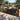 Outdoor patio with a black and orange patterned rug, chairs, and a sofa in a garden setting.